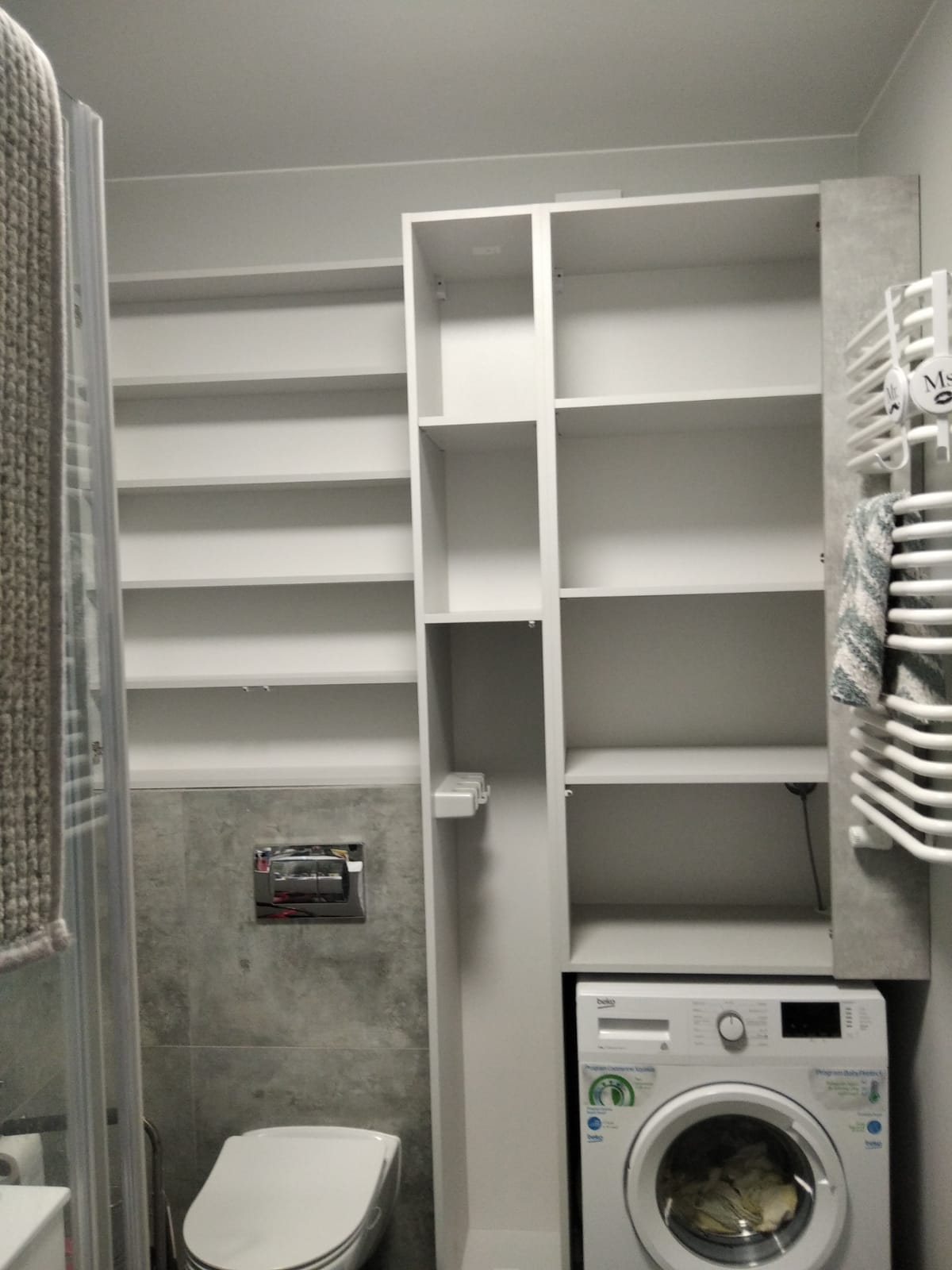 Półki i szafki w łazience z pralką i WC.